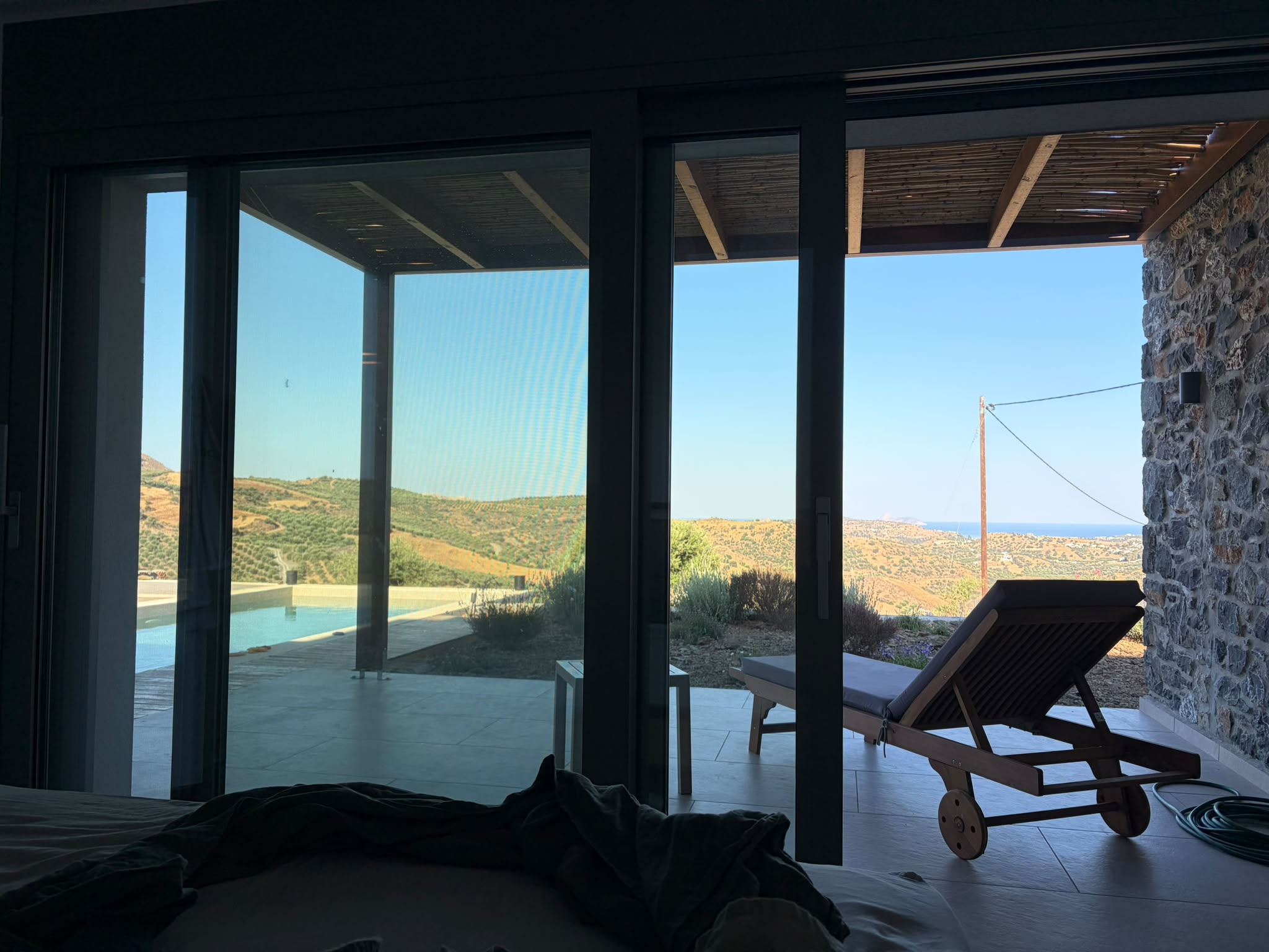 Blick durch die Glasfront eines Hauses auf Kreta über Pool und Landschaft bis zum Meer